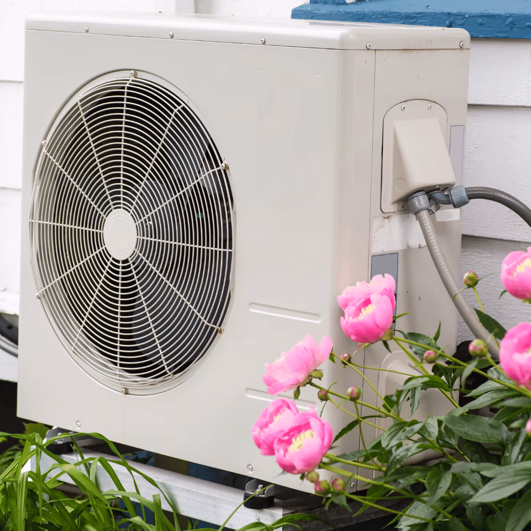 Outdoor heat pump beside a home, with flowers in the foreground