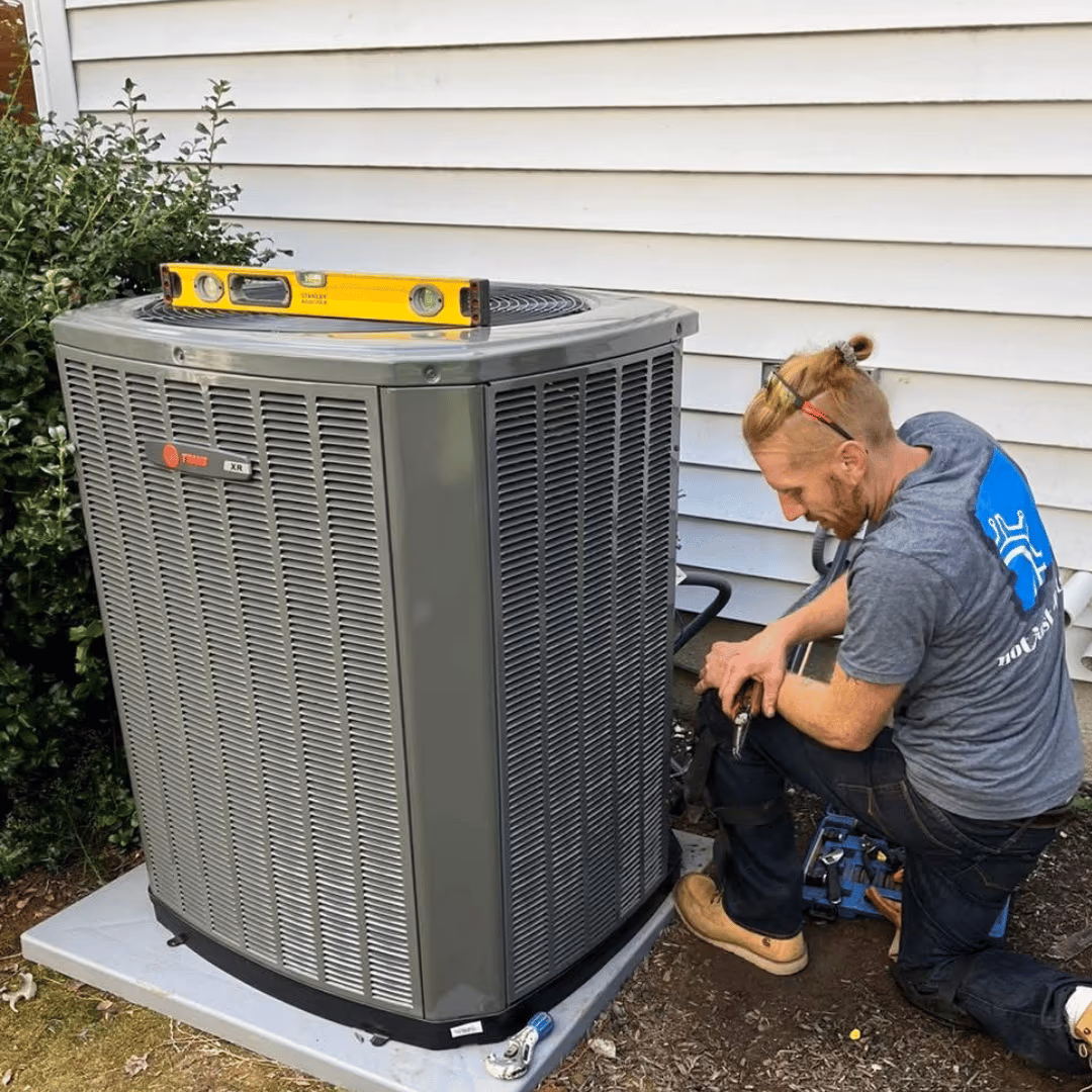 Technician kneeling beside an outdoor air conditioner during a maintenance visit